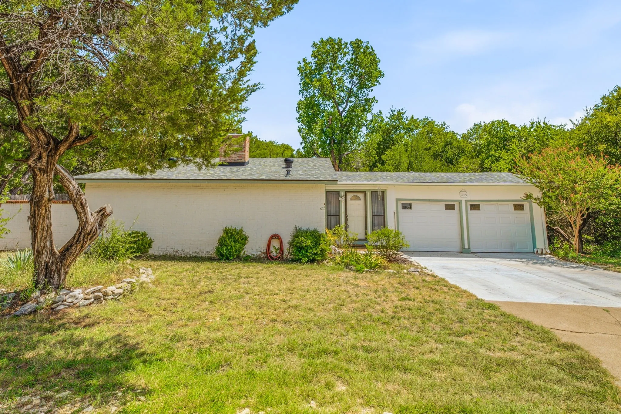 Single-story stucco exterior featuring a two-car garage with individual doors, a front entry with sidelights, and mature trees