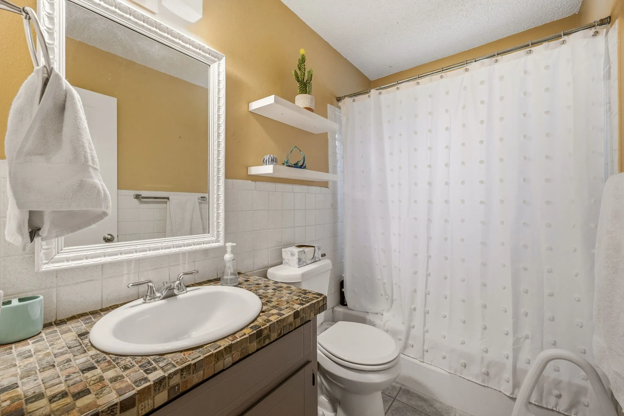 Bathroom featuring a mosaic tile vanity countertop, integrated sink, and framed mirror