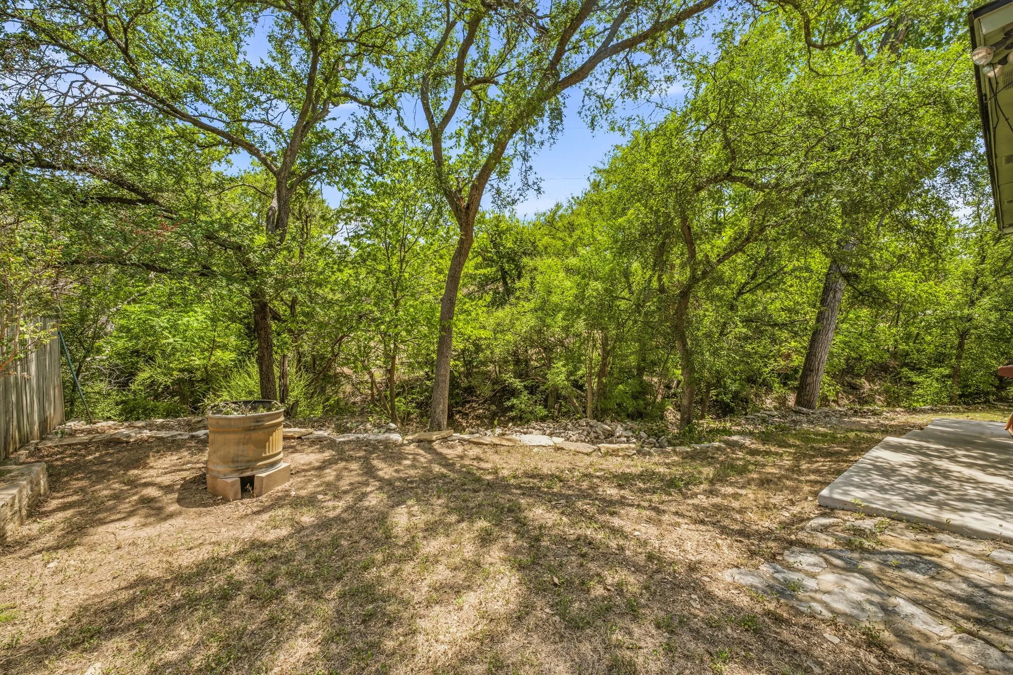 Expansive outdoor space featuring mature trees, a concrete patio, and a built-in stone fire pit
