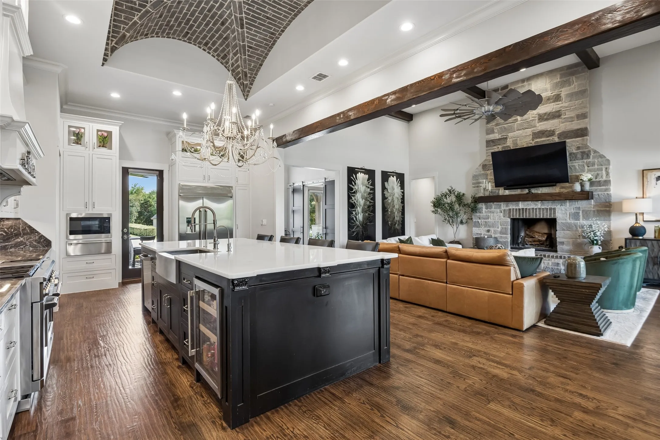 A Strong Visual Connection Between Kitchen and Great Room – The oversized island anchors the open layout, while the brick-vaulted ceiling, exposed beam, and stone fireplace create a seamless transition between the home’s primary gathering spaces.