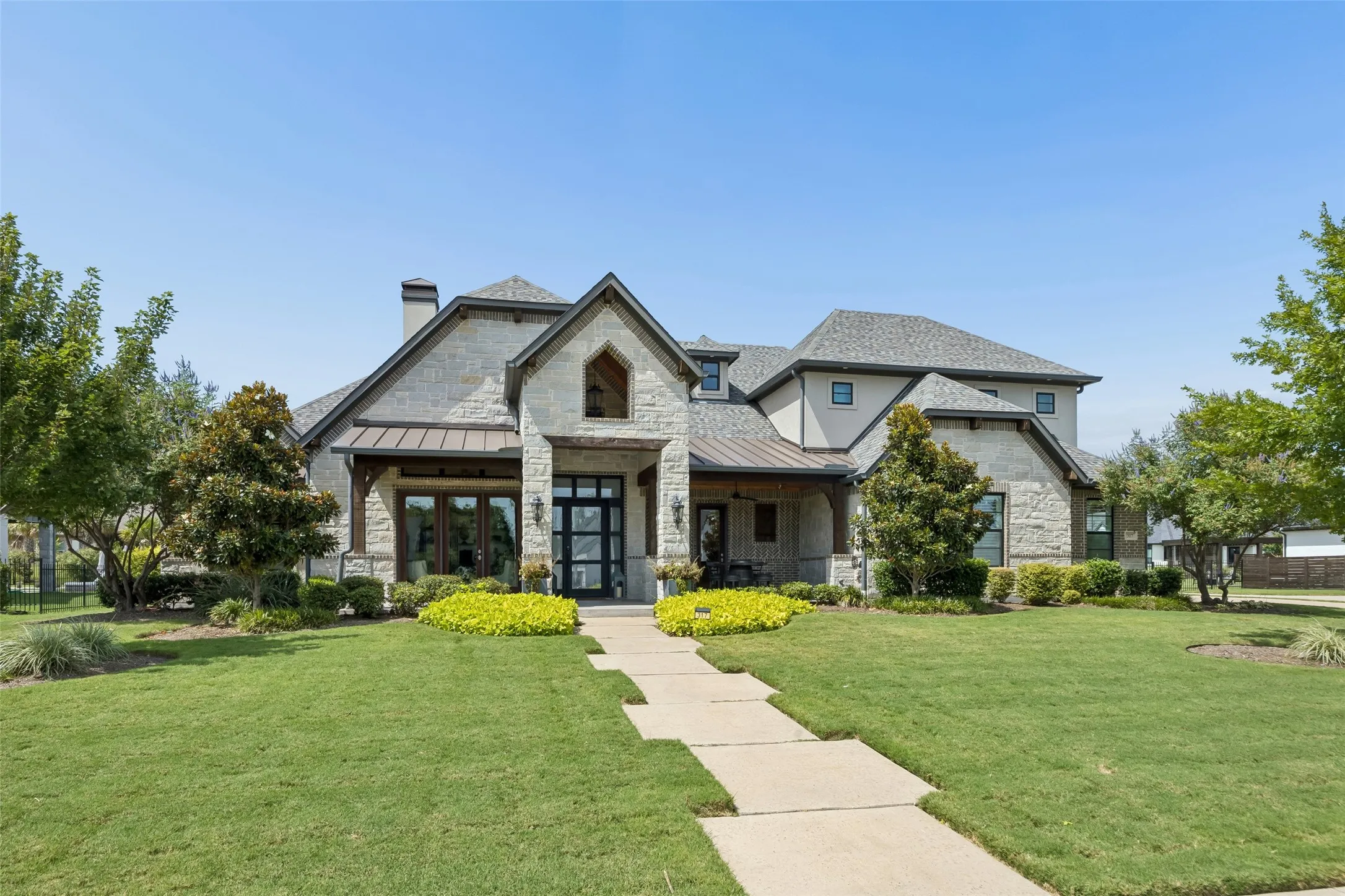 Custom Architecture with Strong Curb Appeal – A striking blend of stone, brick, stucco, metal roofing, and steeply pitched rooflines gives the home a distinctive presence, while the covered entry and mature landscaping create a polished​​‌​​​​‌​​‌‌​‌‌​​​‌‌​‌​‌​‌​​​‌​​ arrival.