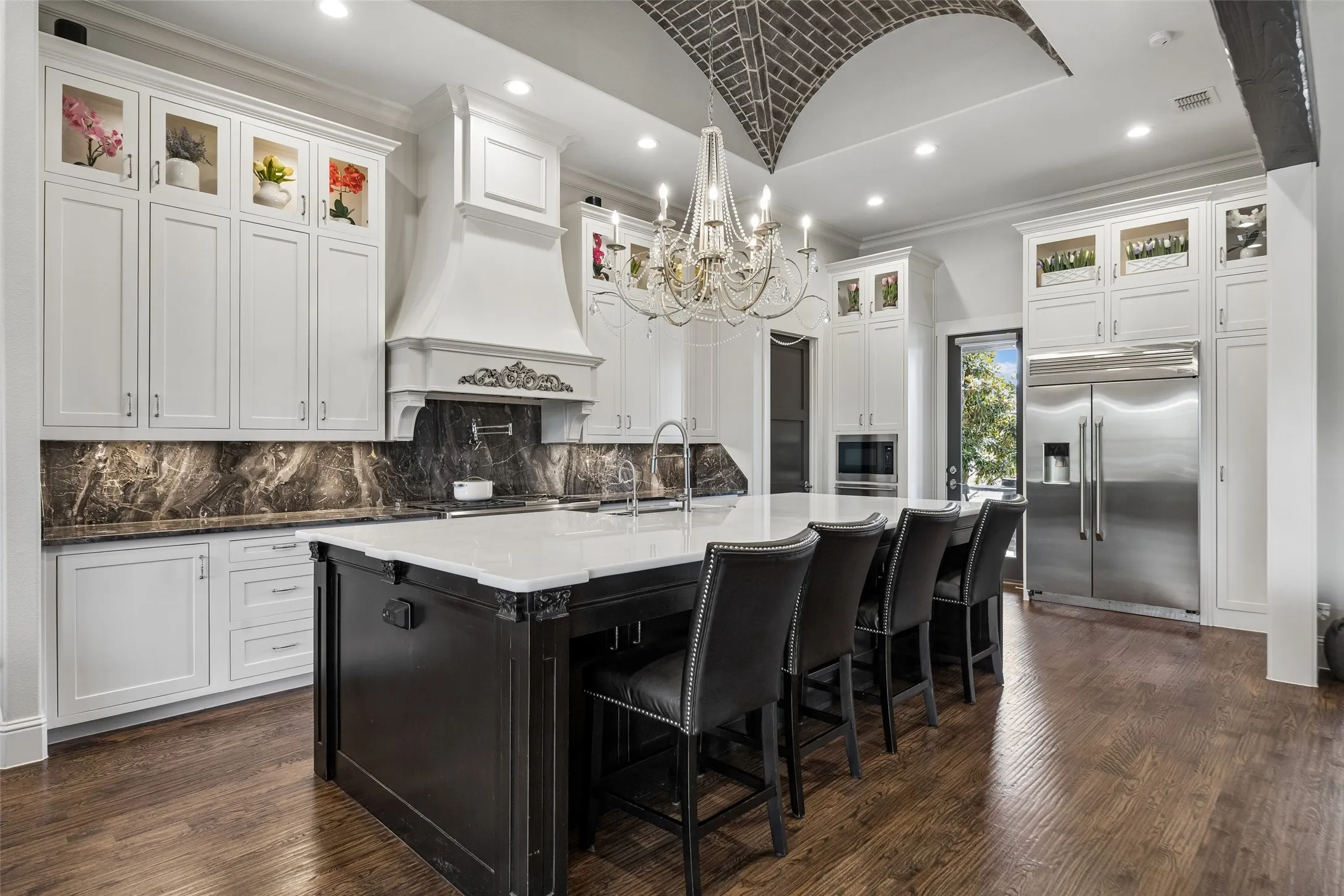 A Statement Kitchen Built for Gathering – An oversized quartz-topped island offers extensive prep space and counter seating, while custom cabinetry, dramatic stone surfaces, and a brick-vaulted ceiling create a kitchen that feels both functional and memorable.