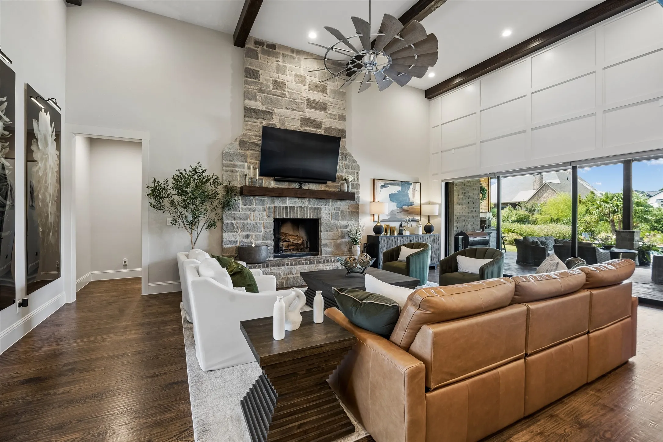 A Great Room Designed Around the View – The spacious living area is anchored by a two-story stone fireplace and framed by exposed beams, while the retractable glass wall extends the room visually and functionally toward the covered terrace and pool.