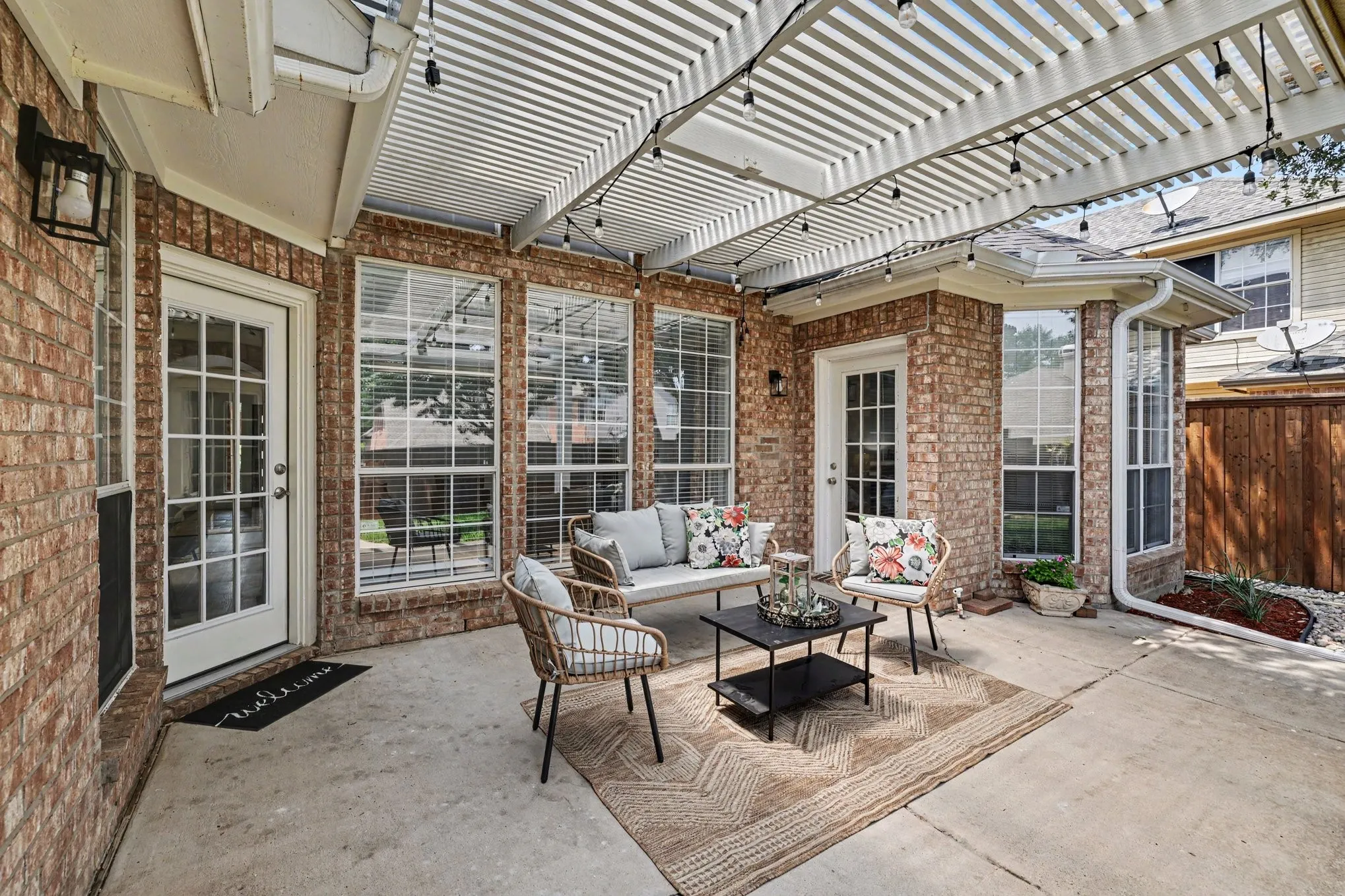 Brick patio featuring a white slatted pergola, multiple large windows, a French-style door, and a concrete surface