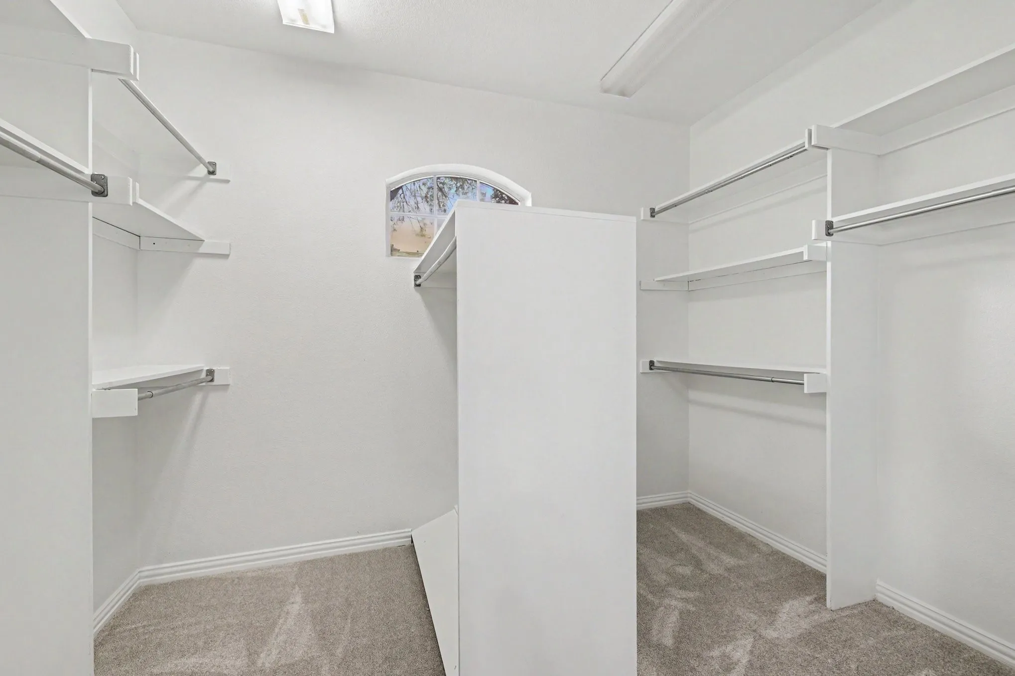 Spacious walk-in closet featuring white built-in shelving, multiple hanging rods, and light-colored carpeting