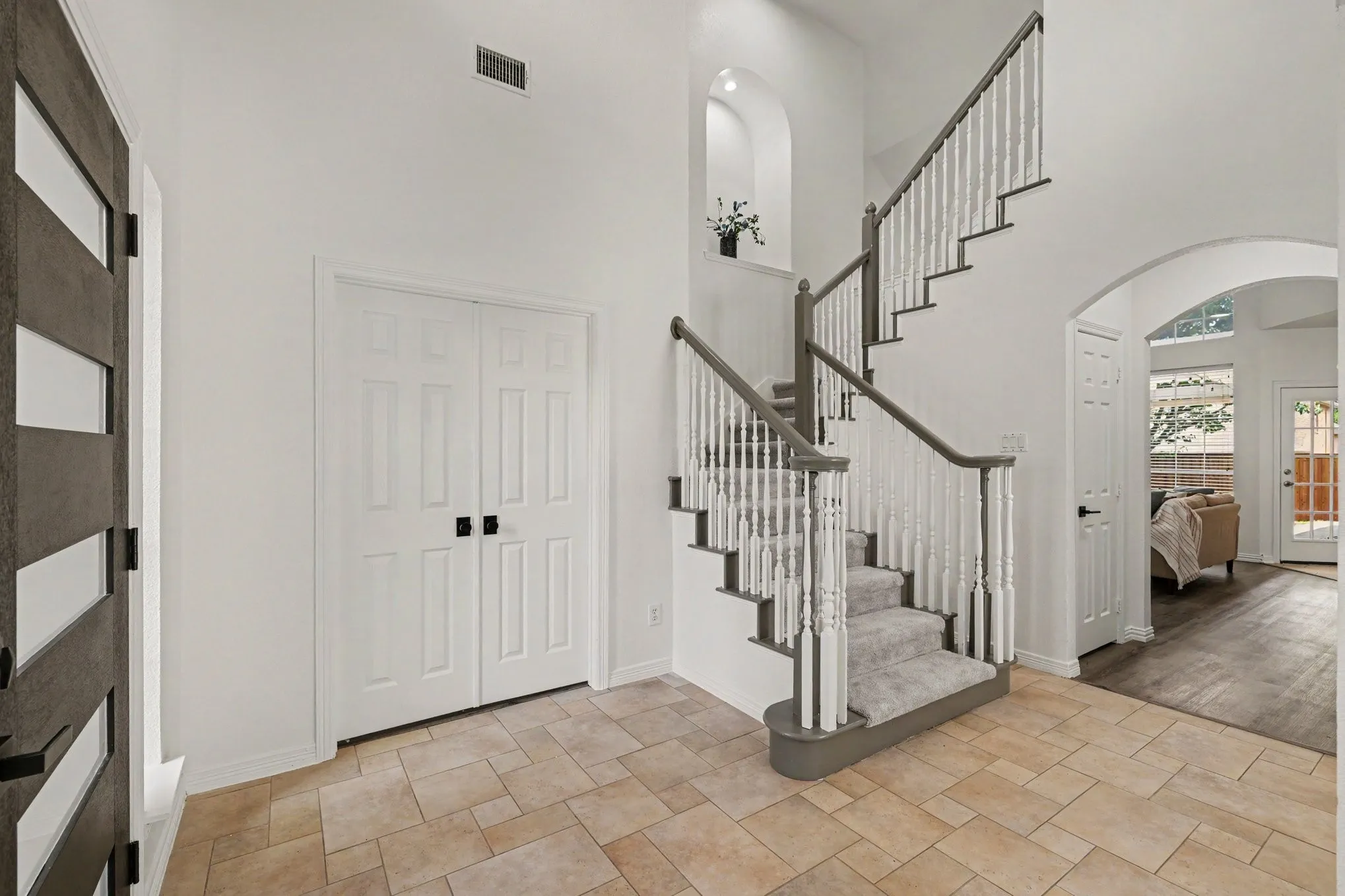 Gracious foyer featuring a carpeted staircase with painted spindles and dark handrails, arched entryway, and neutral tile flooring