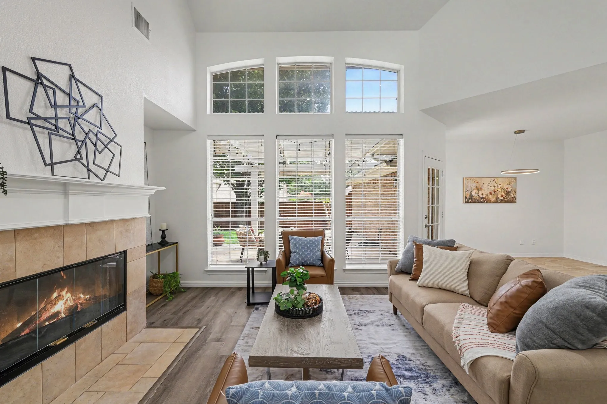 Living area featuring a floor-to-ceiling tiled fireplace, large windows with arch-top transoms, wood-finish flooring, and a vaulted ceiling