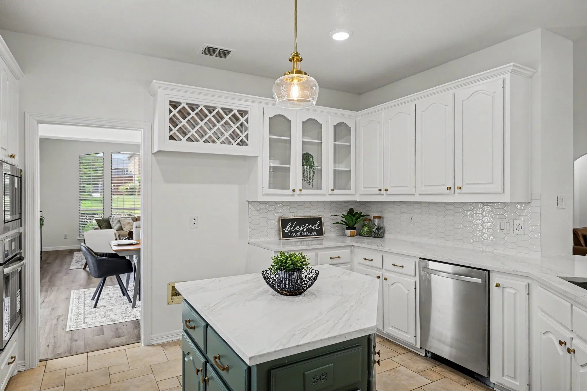 Kitchen featuring an island with a light-toned countertop, white cabinetry with gold-toned hardware, a white hexagonal tile backsplash, and stainless steel appliances