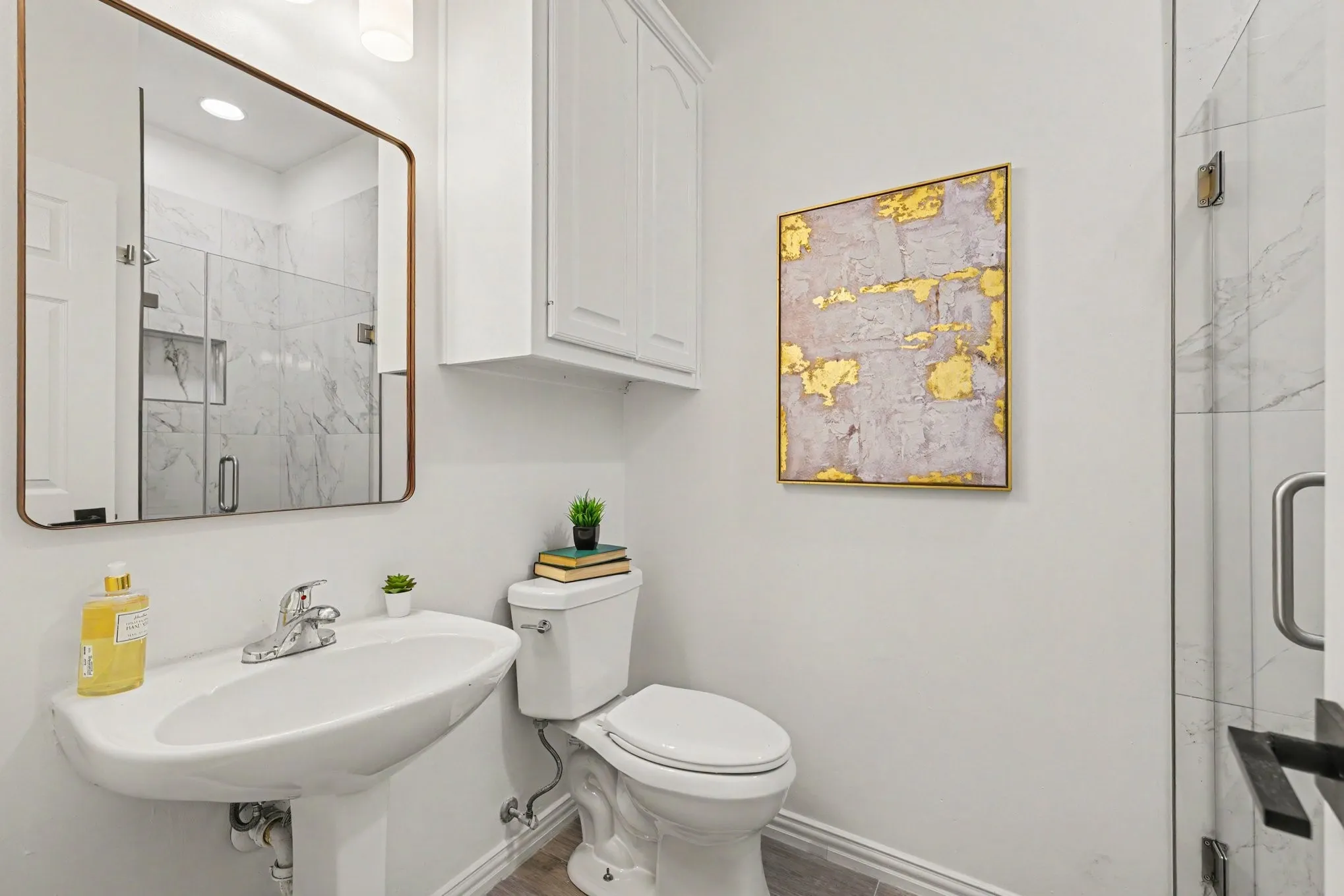 Pedestal sink with chrome faucet, large framed mirror, and built-in white cabinetry