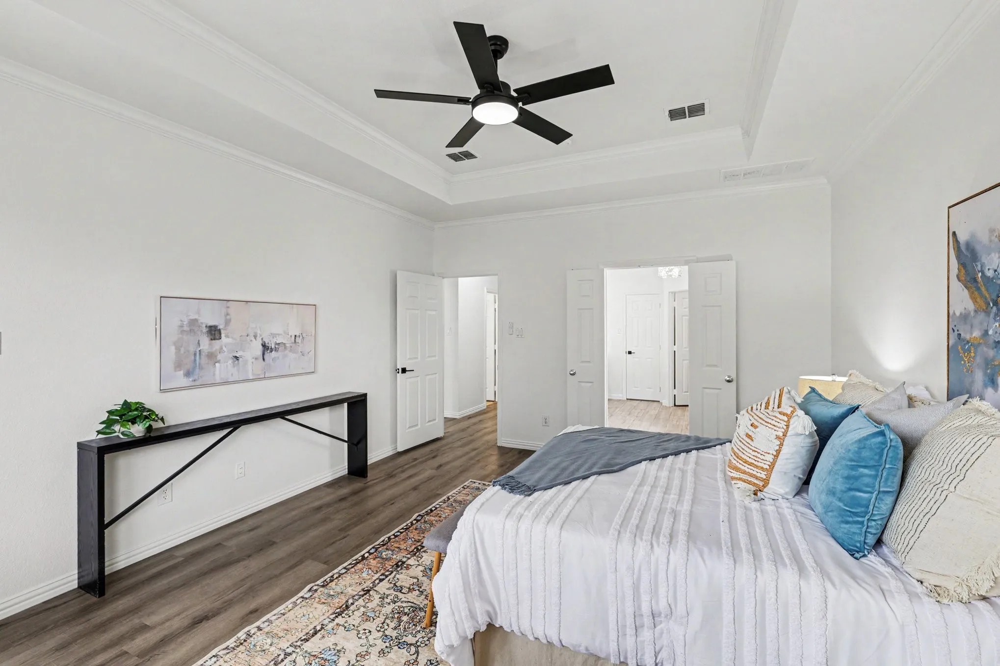 Spacious room featuring wood-finish flooring, a tray ceiling, and a ceiling fan with integrated lighting