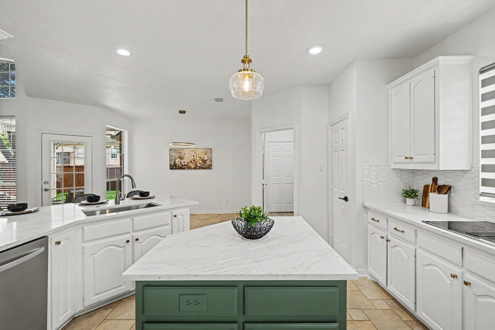 Bright kitchen featuring a green-accented island with a white stone countertop, white cabinetry with gold-tone hardware, a stainless steel dishwasher, and a white hexagonal tile backsplash