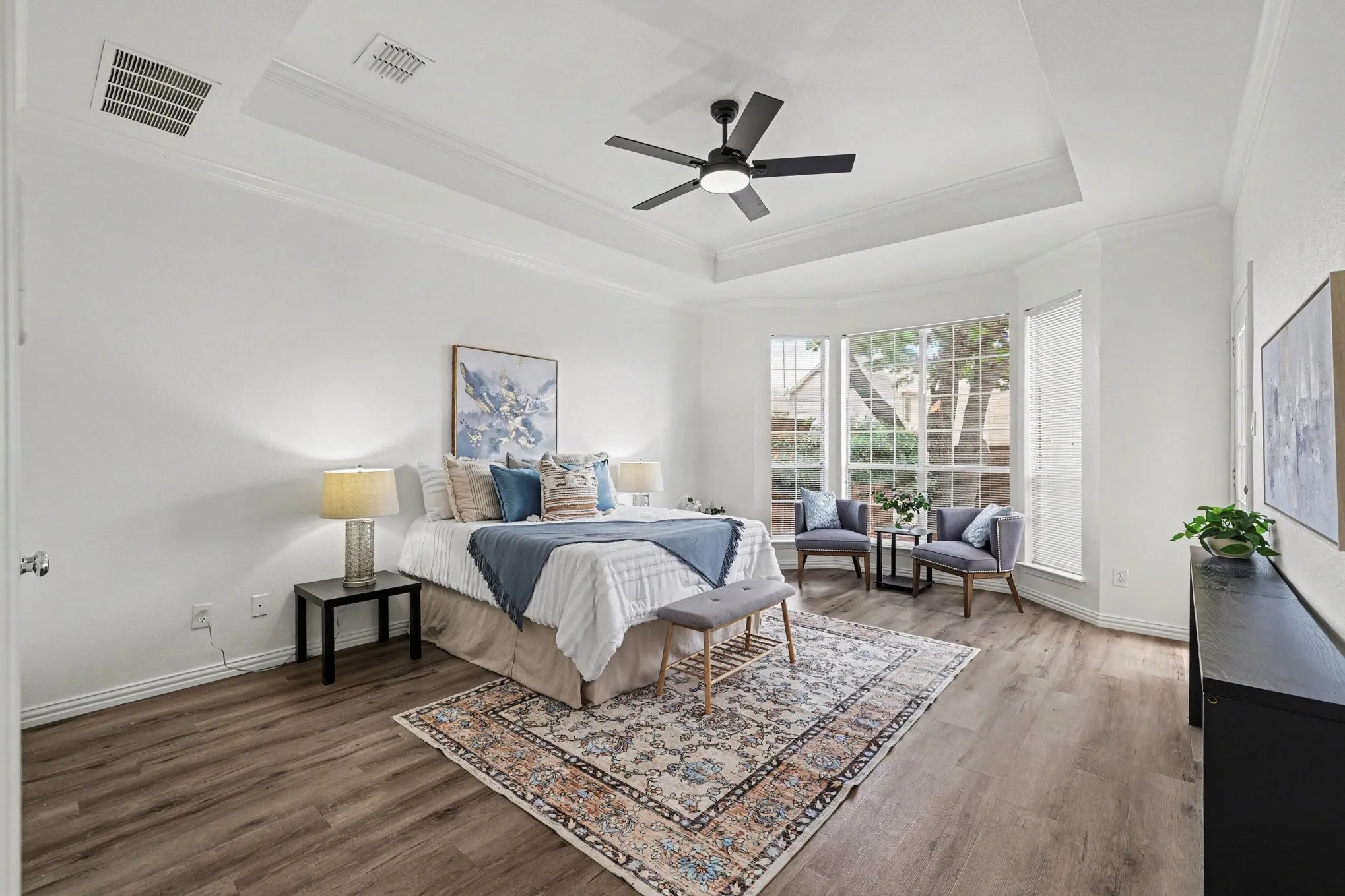 Spacious room featuring wood-finish flooring, a tray ceiling with a black ceiling fan, and large bay windows