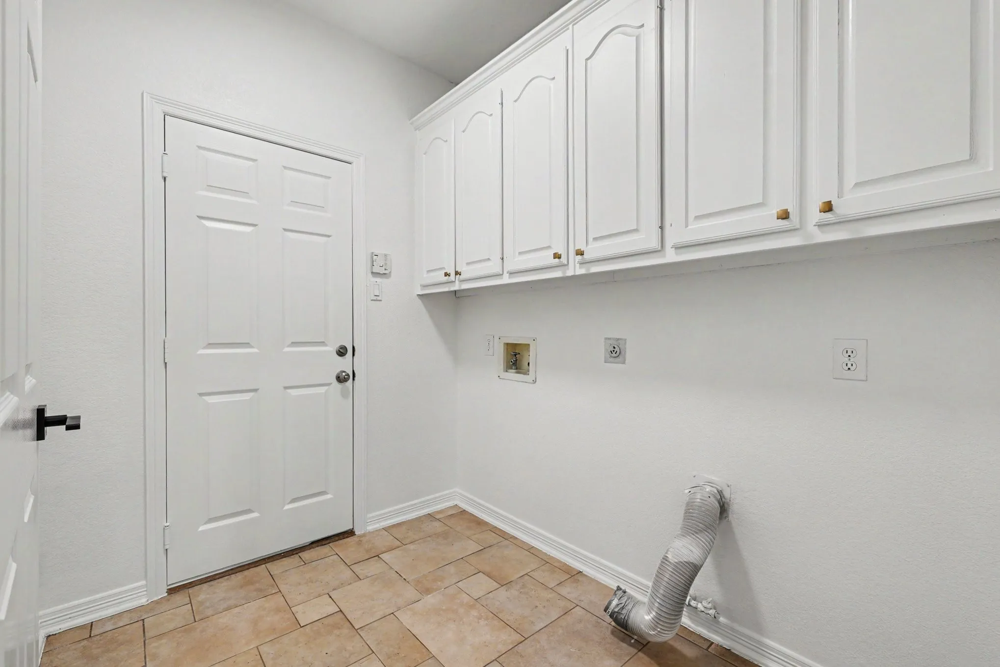 Utility area featuring upper cabinetry with gold-tone hardware, a paneled door, and neutral-toned tile flooring