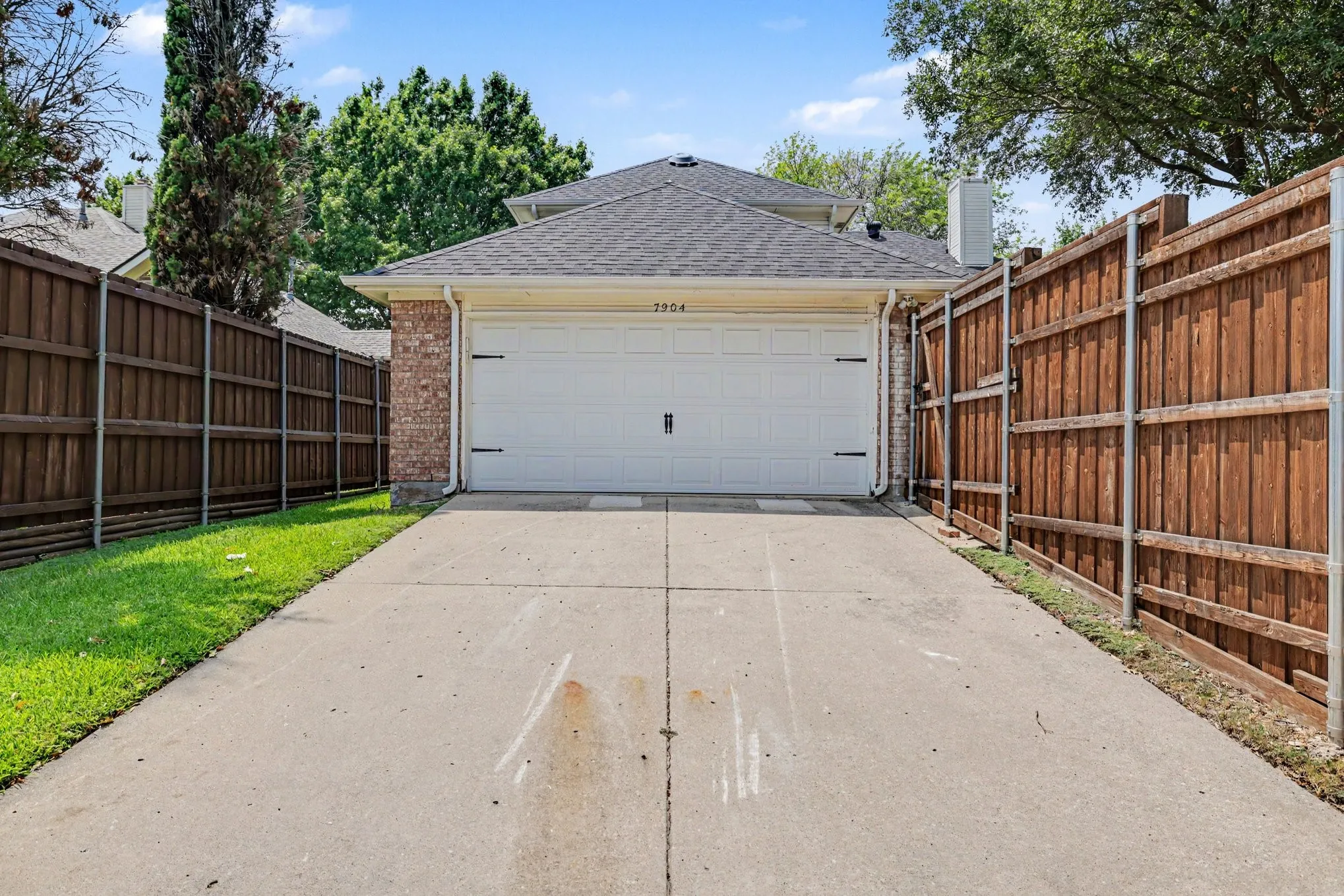 Two-car garage with a white door and decorative hardware, brick facade, and a shingled roofline