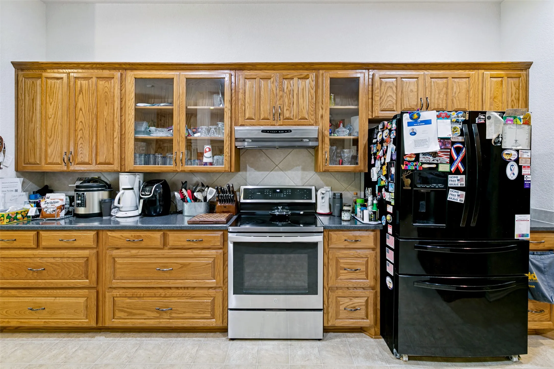 Kitchen featuring extensive wood cabinetry, dark countertops, a stainless steel range, and a tile backsplash