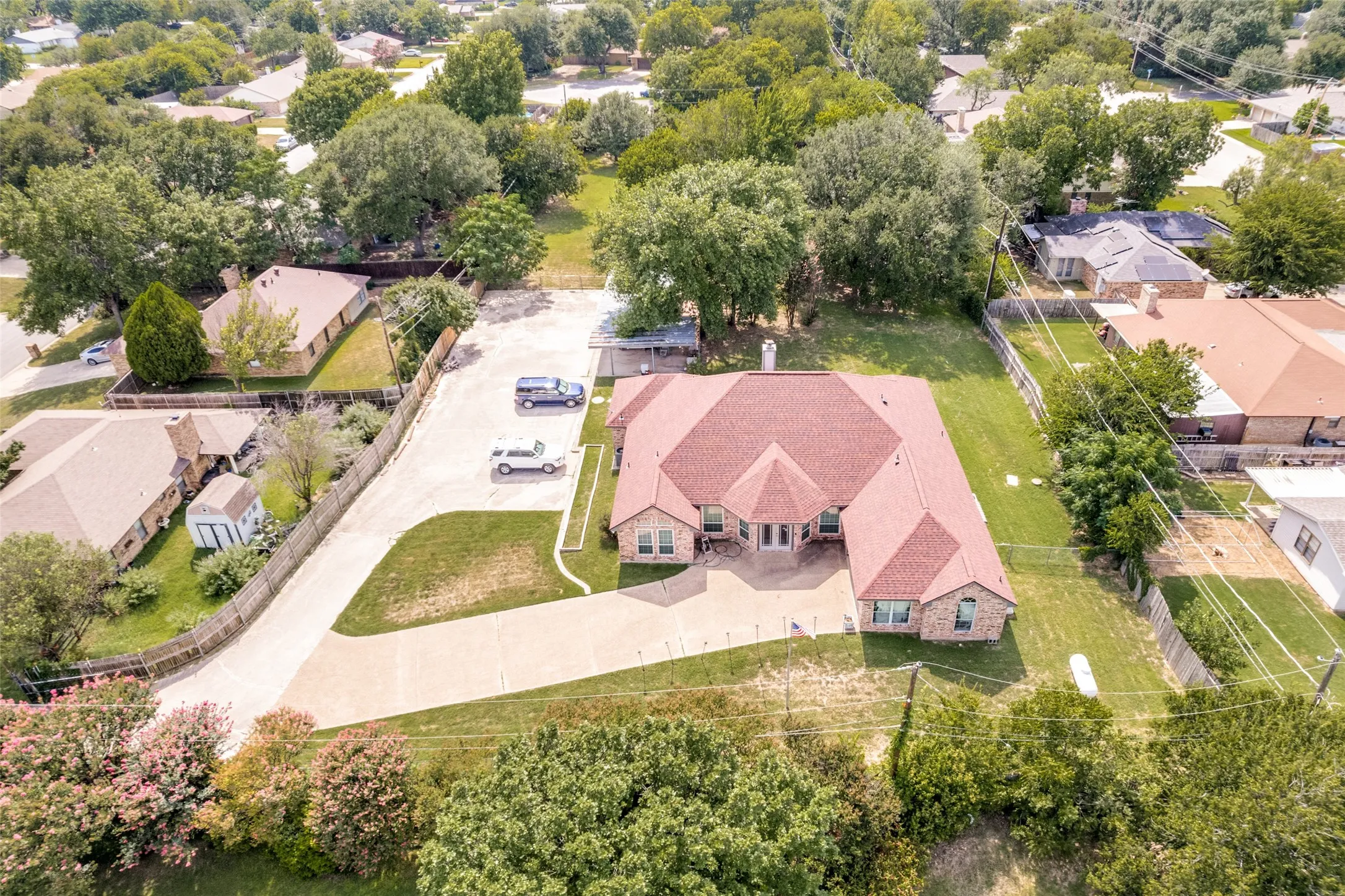 Spacious property featuring a large brick exterior, a red shingle roof, a generously sized concrete driveway, and surrounding mature​​‌​​​​‌​​‌‌​‌‌​​​‌‌​‌​‌​‌​​​‌​​ trees