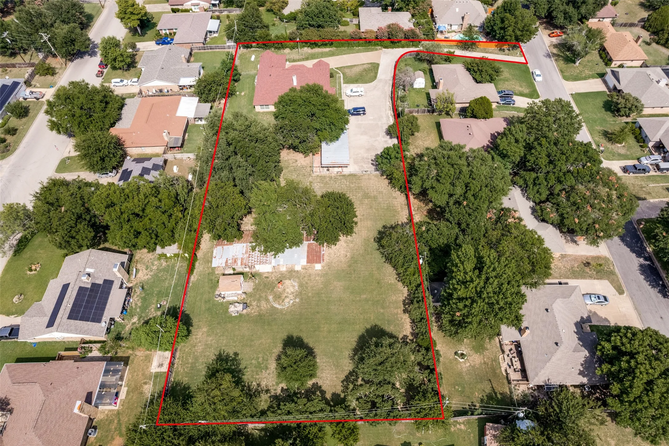 Expansive property outlined by a distinct red boundary, featuring a central building with a red tile roof, surrounded by mature trees and verdant open spaces