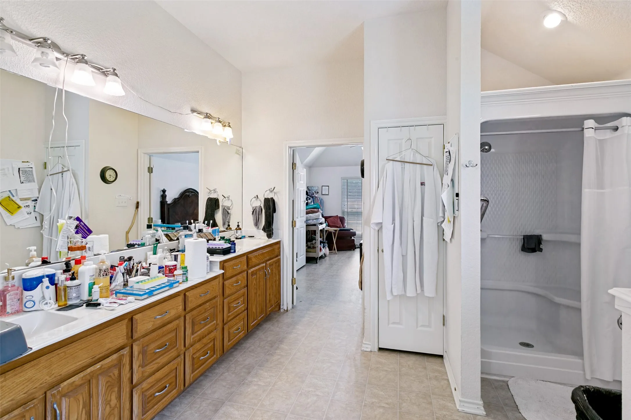 Spacious bathroom featuring a dual vanity with wood cabinetry, a large integrated mirror, overhead bar lighting, and a white shower enclosure
