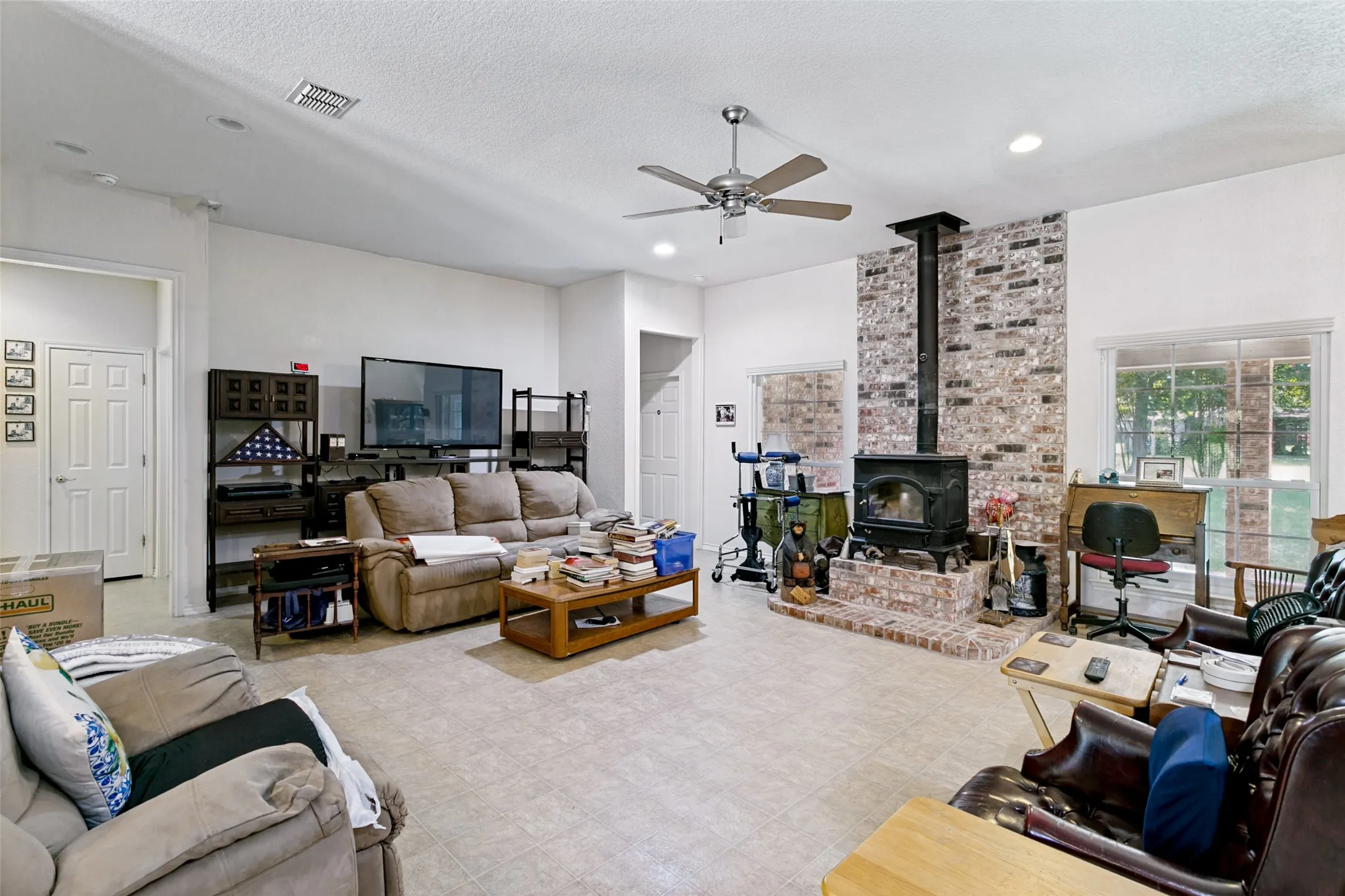 Spacious living area featuring light-toned flooring,  wood-burning stove with a raised hearth, and a ceiling fan