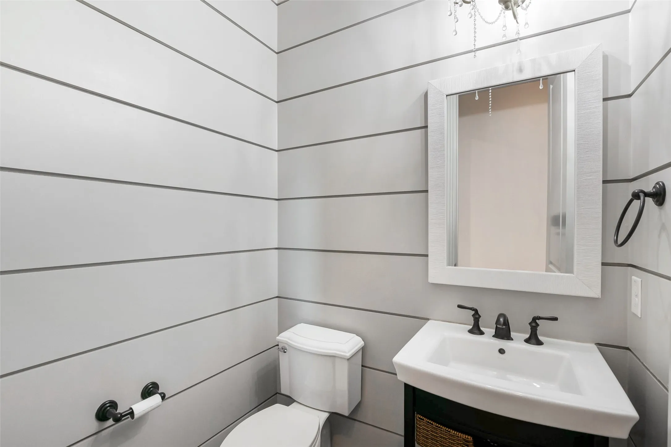 Powder room featuring shiplap walls, a corner vanity with a white basin sink, a framed mirror, and a decorative chandelier