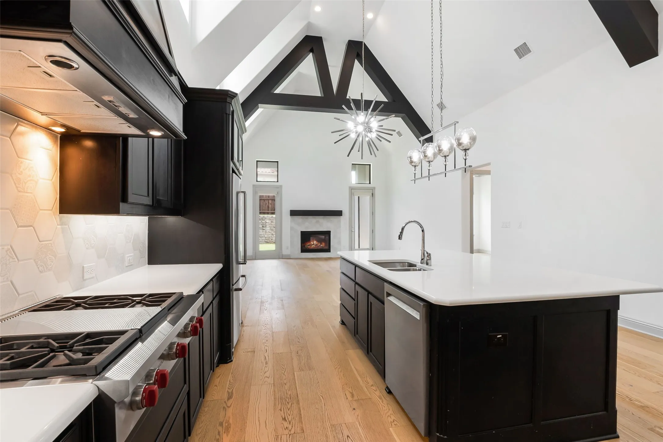 Open-concept kitchen featuring dark cabinetry, white countertops, hexagon tile backsplash, and a large central island with an undermount sink