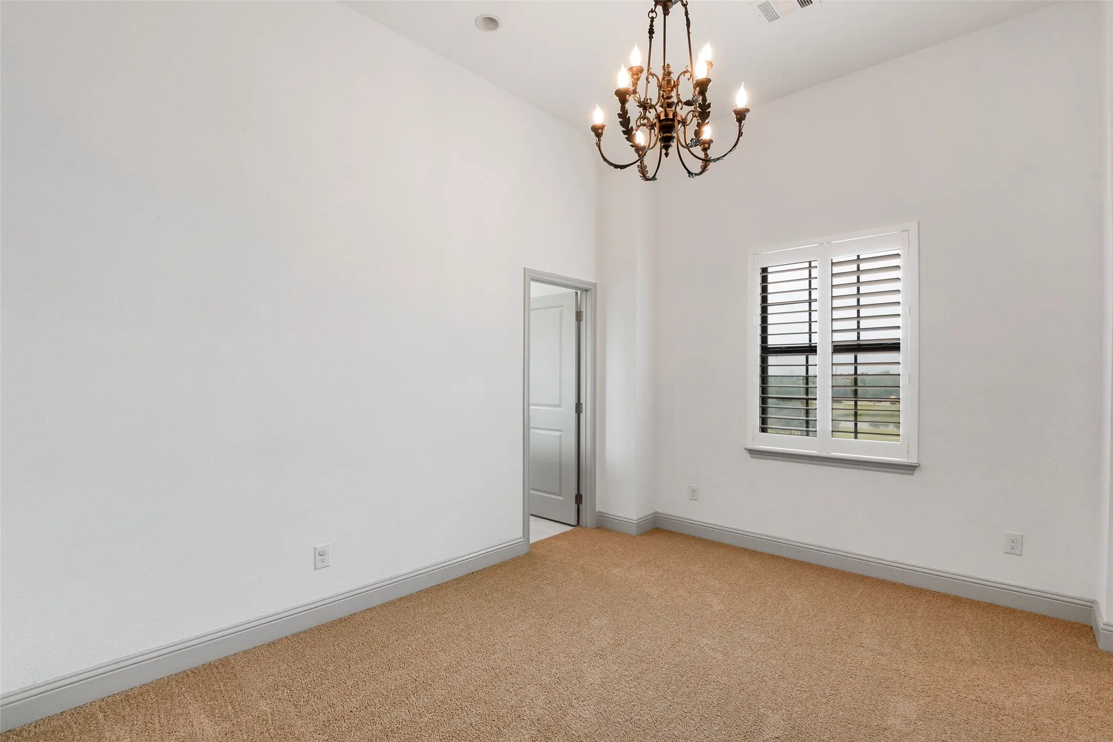 Room featuring high ceilings, a decorative chandelier, and light-colored carpeting