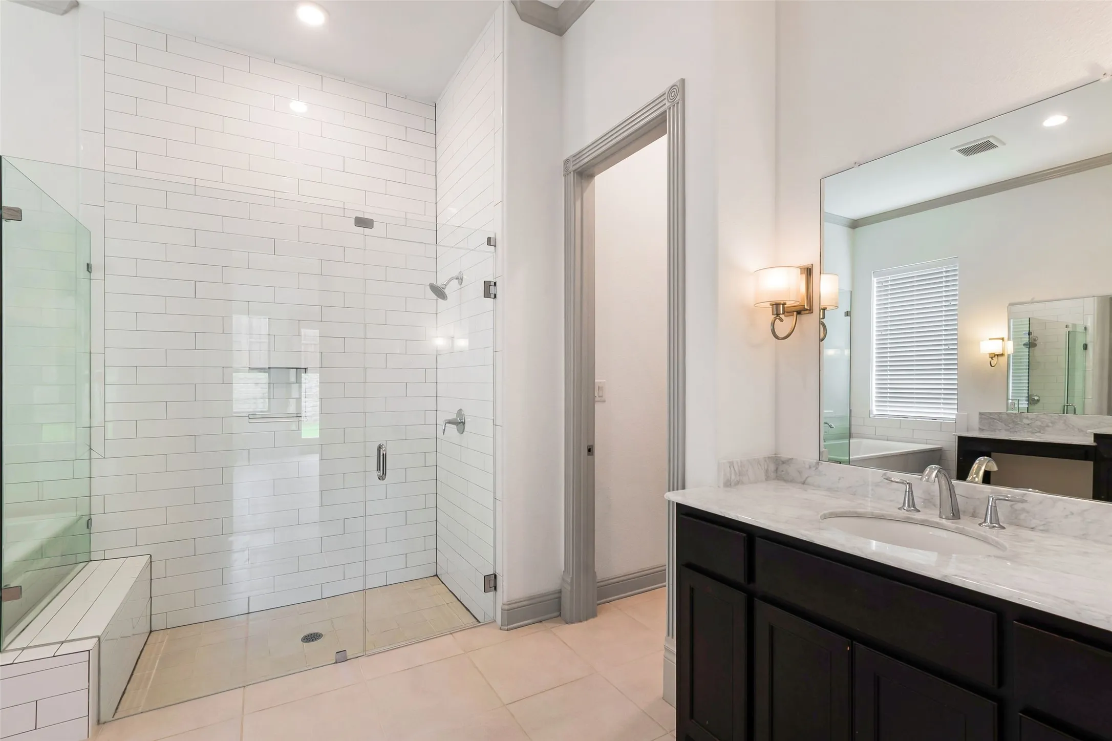 Spacious bathroom featuring a glass-enclosed shower with white subway tile, a built-in shower bench, and a dual shower head system