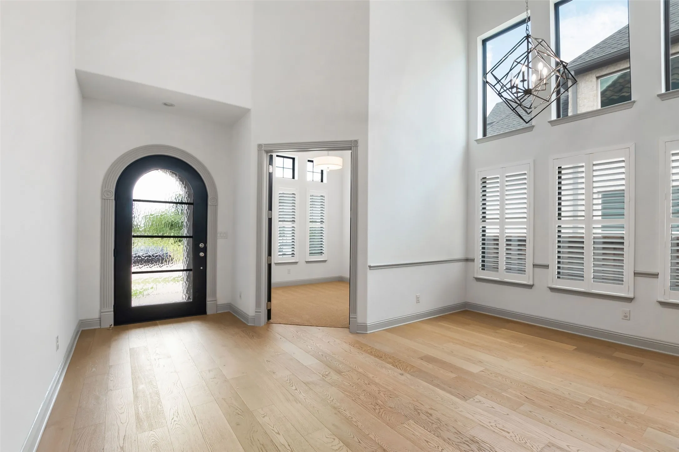 Two-story foyer featuring an arched entryway with a glass-paneled door, tall ceilings, ight LVP flooring, , and a modern geometric chandelier
