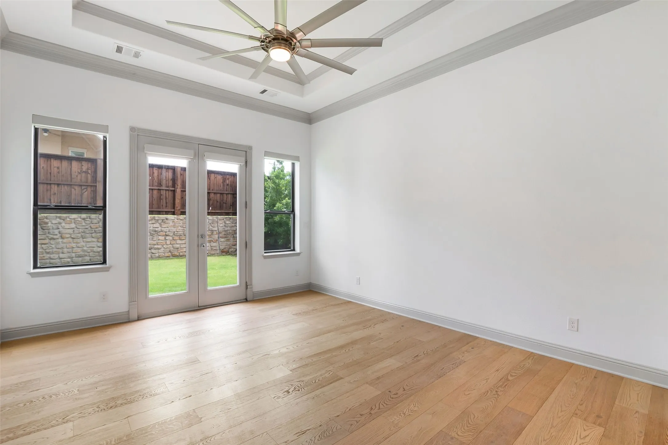 Recessed tray ceiling with crown molding, contemporary ceiling fan, light LVP flooring, and double French doors opening to the backyard