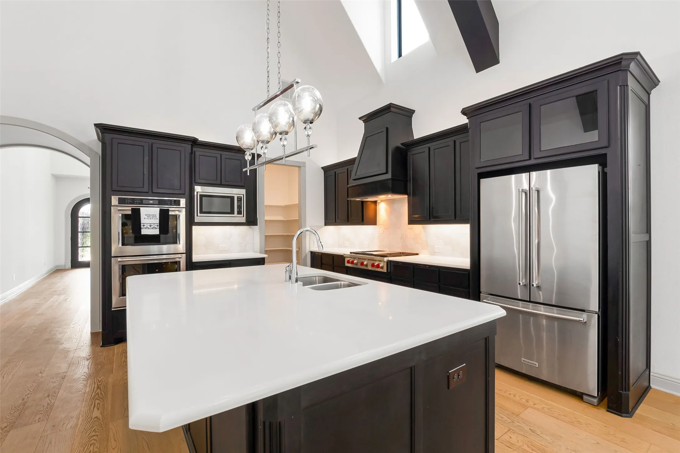 Kitchen featuring a large central island with a white countertop and double sink, dark cabinetry, stainless steel appliances, and ight LVP flooring