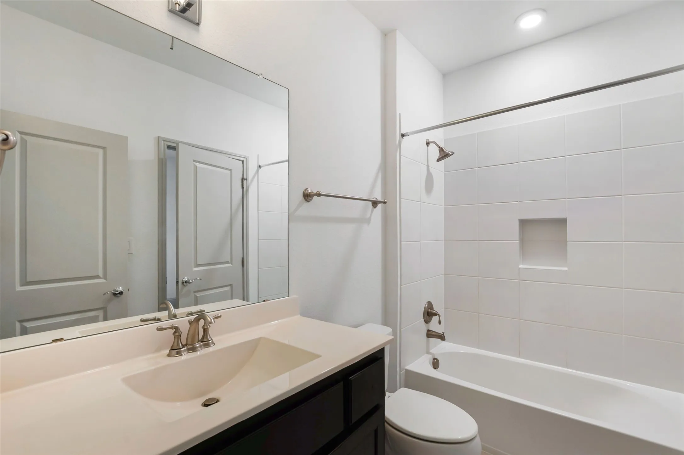 Bathroom featuring a dark wood-finish vanity with an integrated sink, a large wall-mounted mirror, and a tub with white subway tile surround and a recessed niche