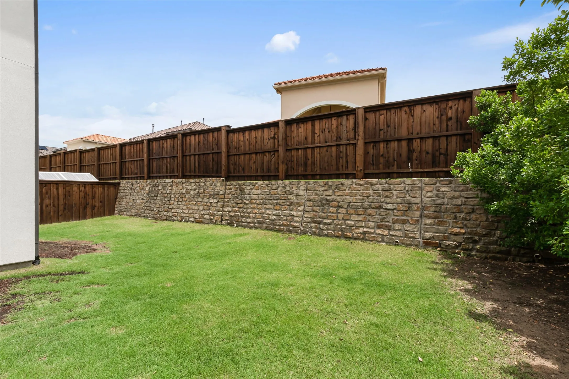 Grassy backyard featuringi a stone retaining wall and a dark wood privacy fence