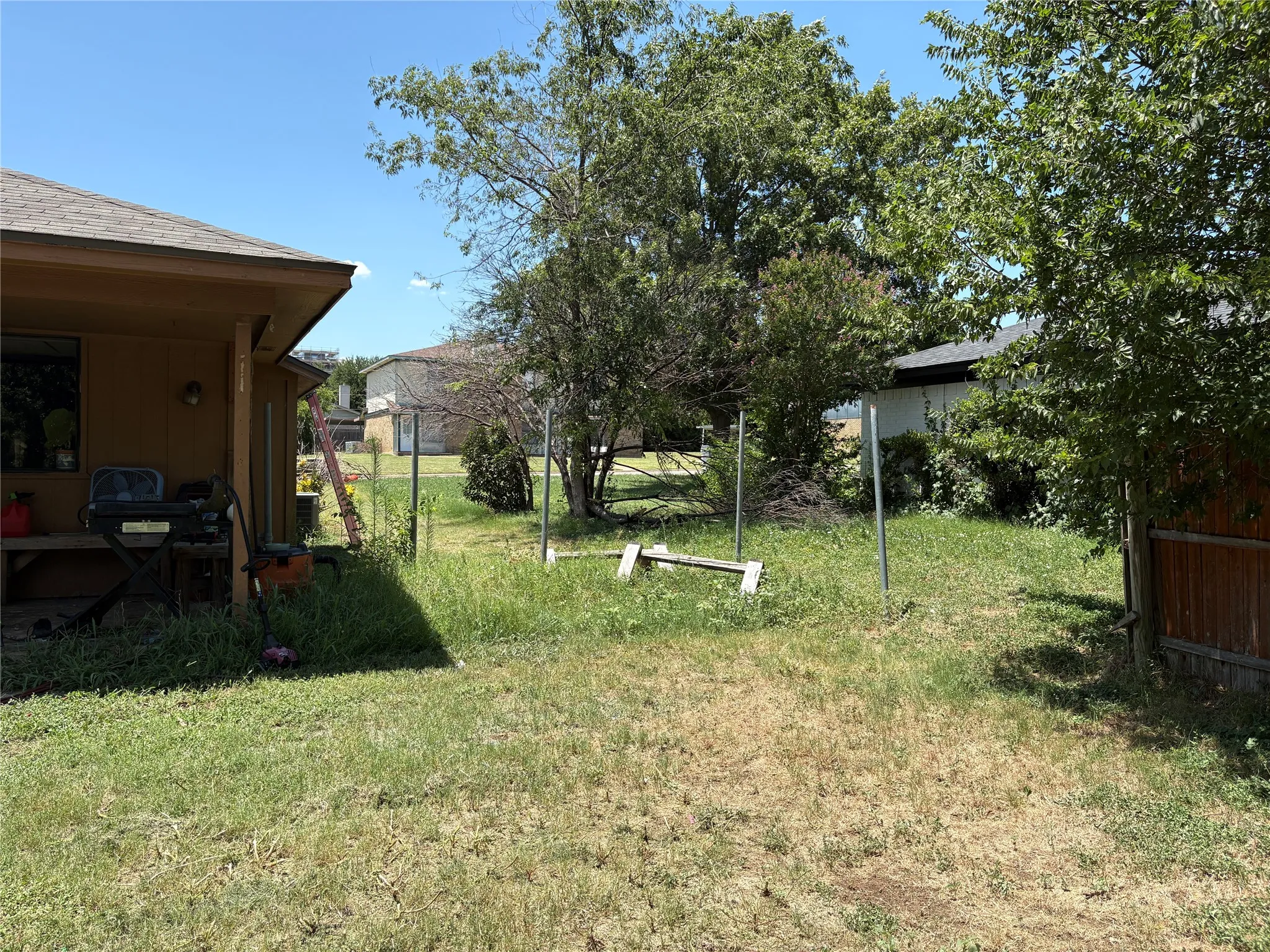 Grassed backyard featuring mature trees, a partial privacy fence, and a covered patio area