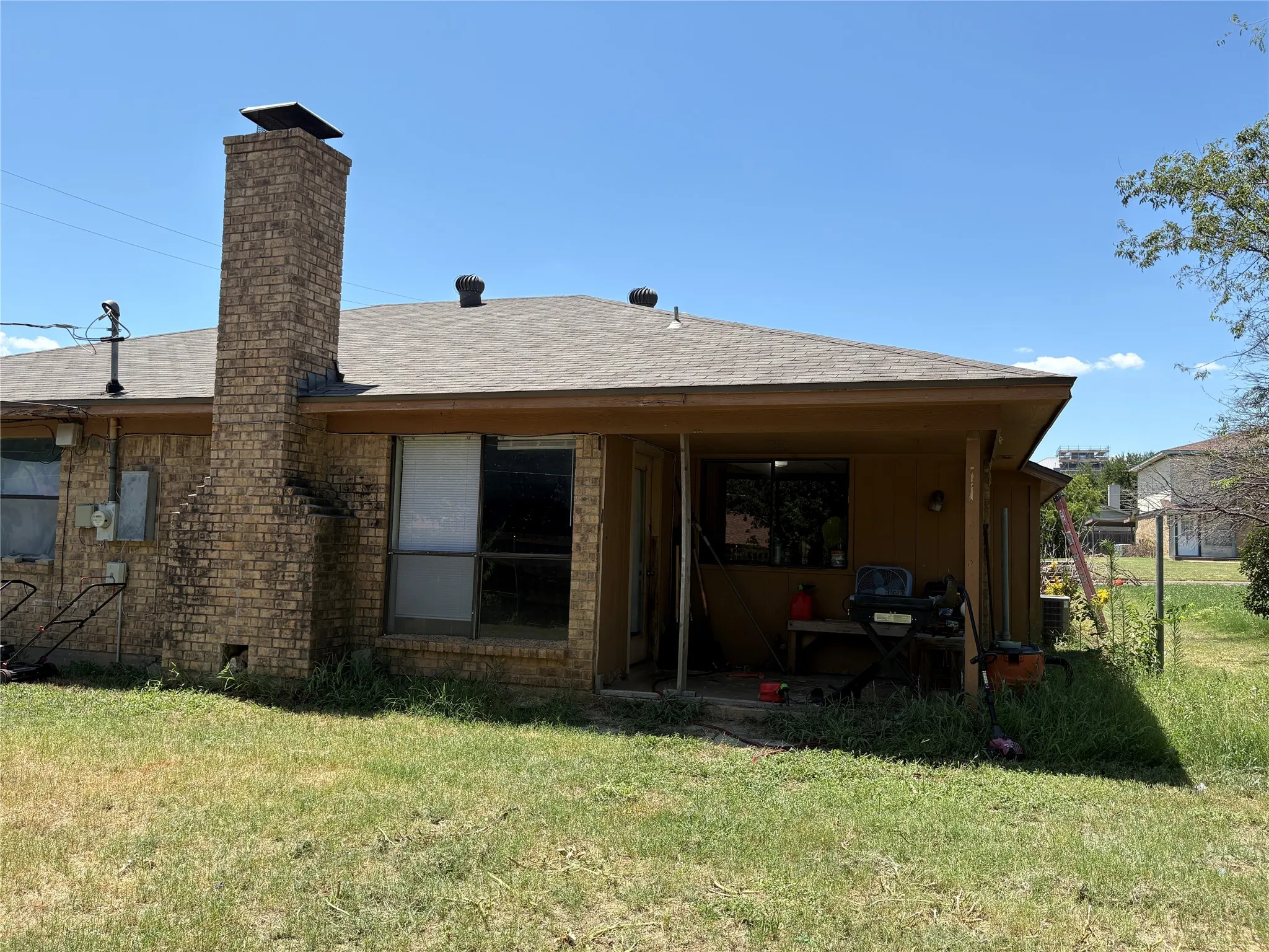 Rear exterior featuring a brick chimney, covered patio, and shingle roofing