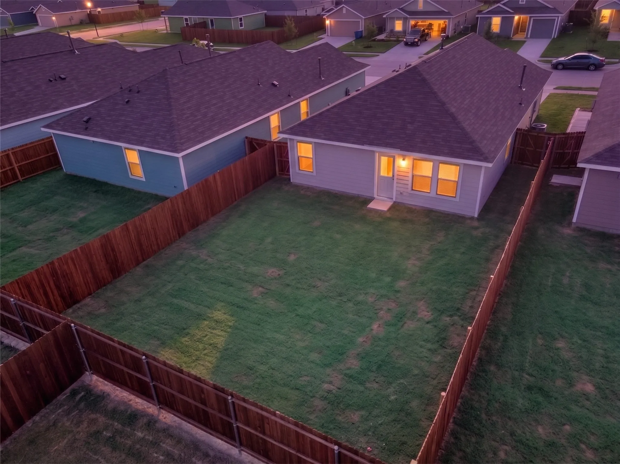 Spacious backyard featuring a full privacy fence, manicured lawn, and a light-colored exterior with multiple windows