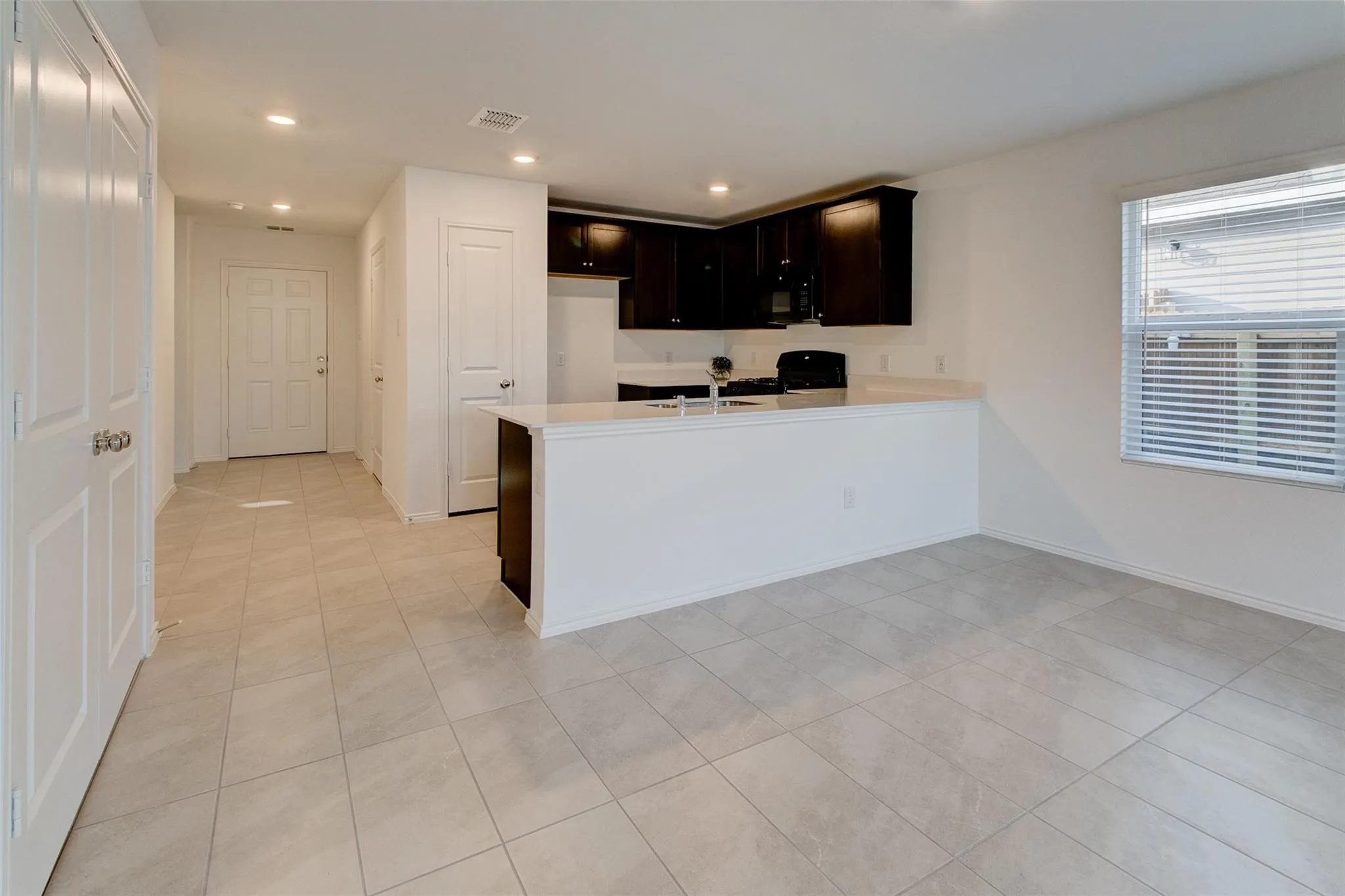 Open-concept layout featuring light-toned tile flooring, recessed lighting, and a kitchen with dark wood cabinetry