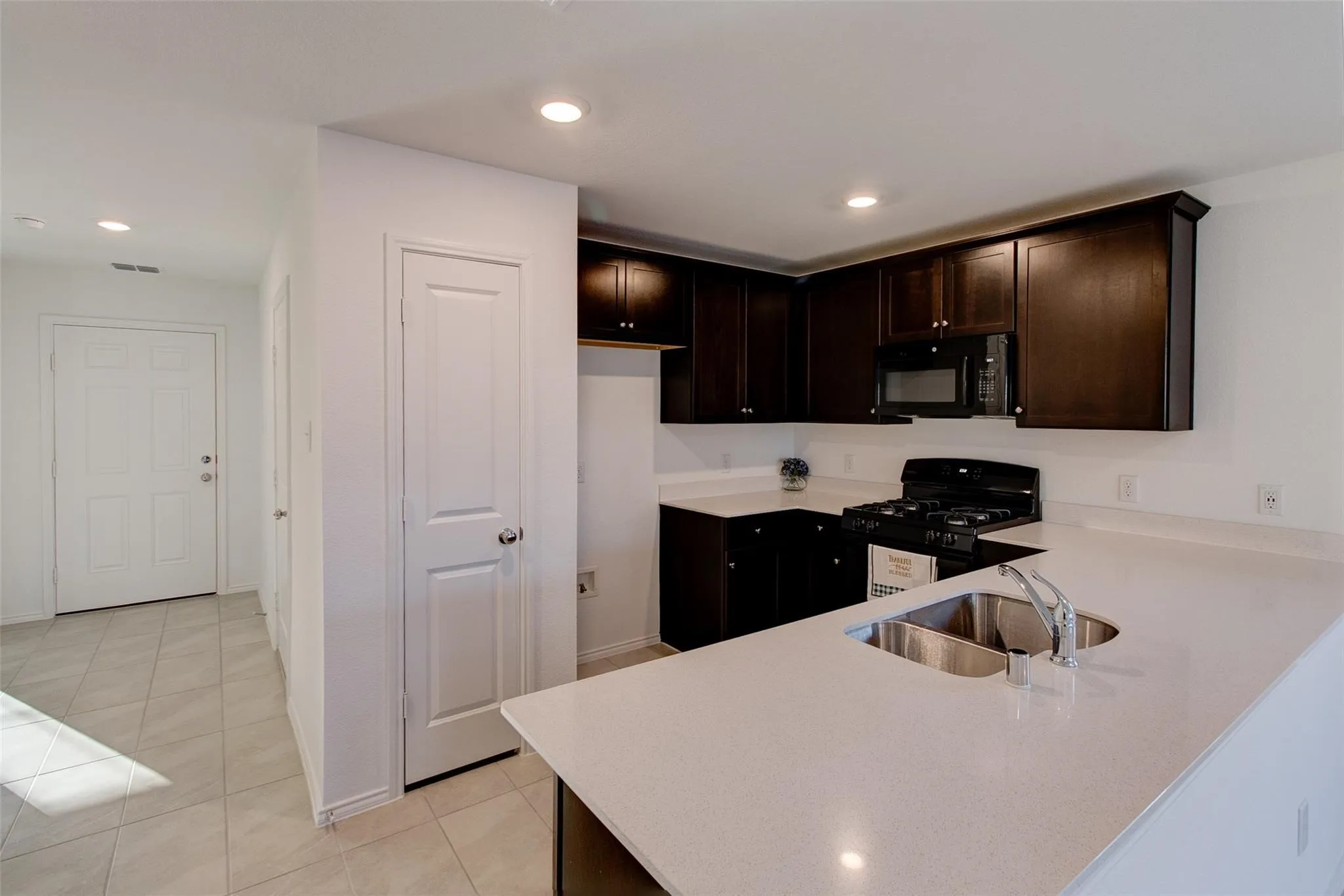 Kitchen featuring dark wood cabinetry, light-toned countertops, and a double basin stainless steel sink with a gooseneck faucet
