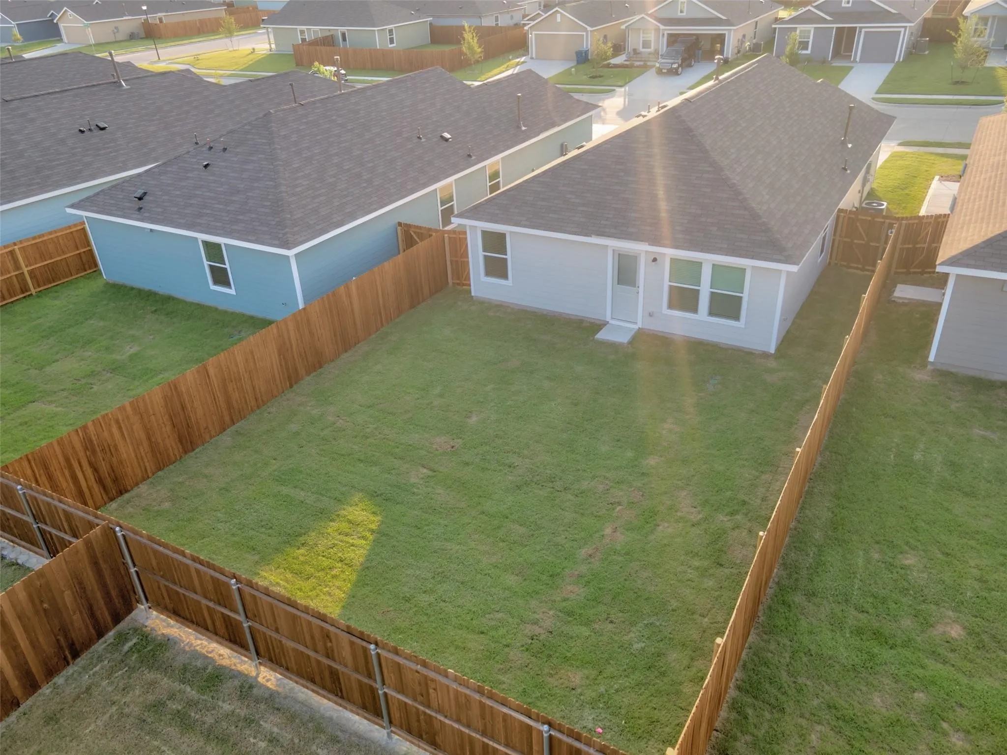 Spacious, fenced backyard featuring a manicured lawn, light gray exterior siding, white trim, a rear entry door, and multiple windows