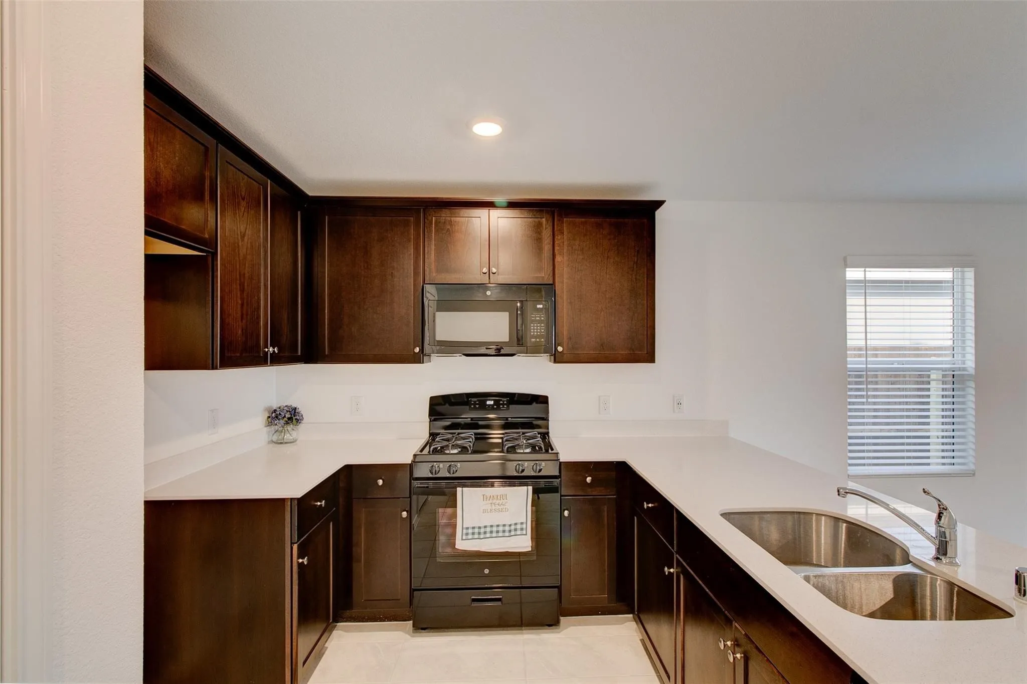 U-shaped kitchen featuring dark wood cabinetry, light countertops, a double basin stainless steel sink with a gooseneck faucet, a built-in microwave, and a gas range