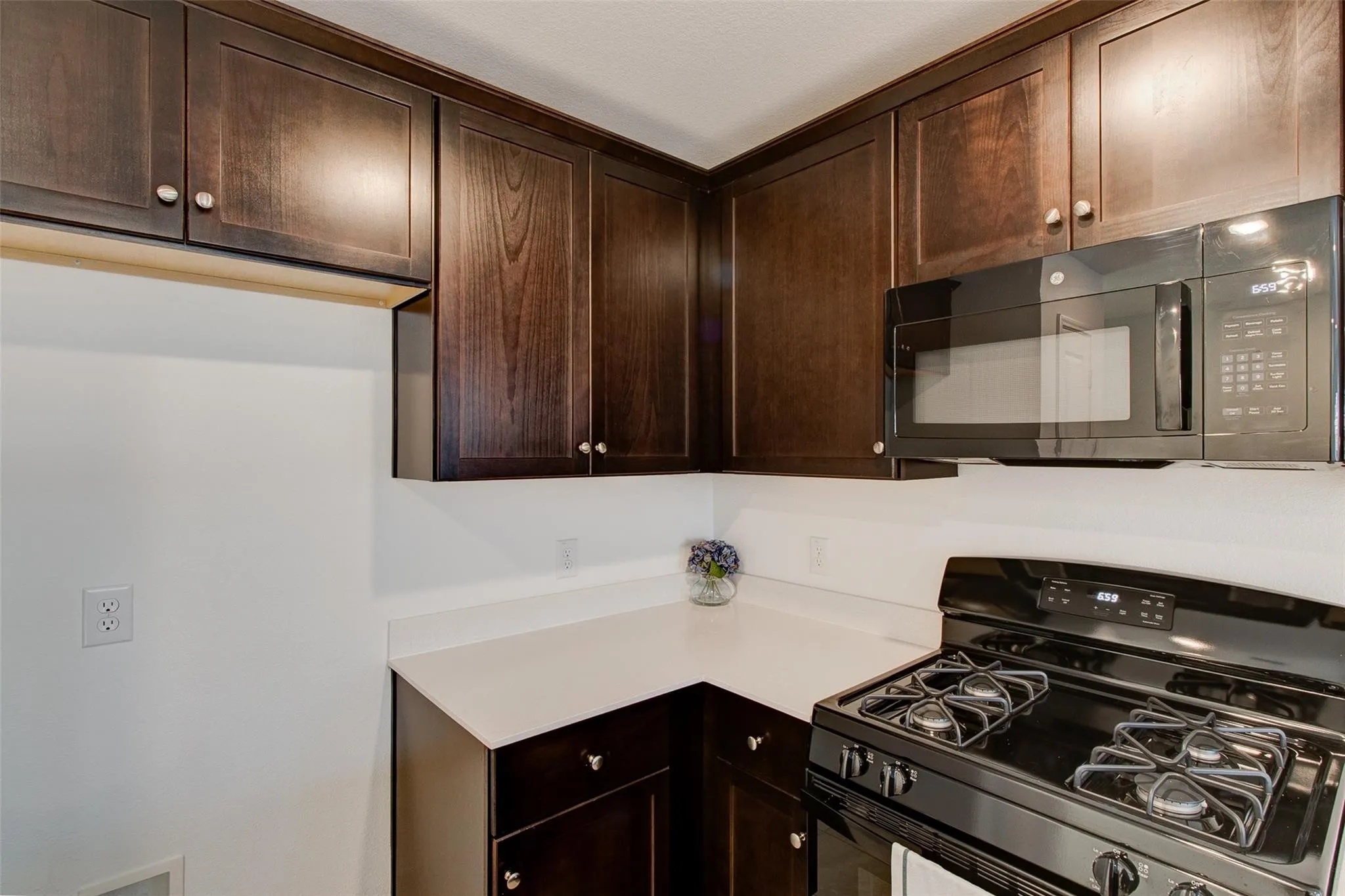 Kitchen featuring dark wood-finish cabinetry, light countertops, an over-the-range microwave, and a black gas range