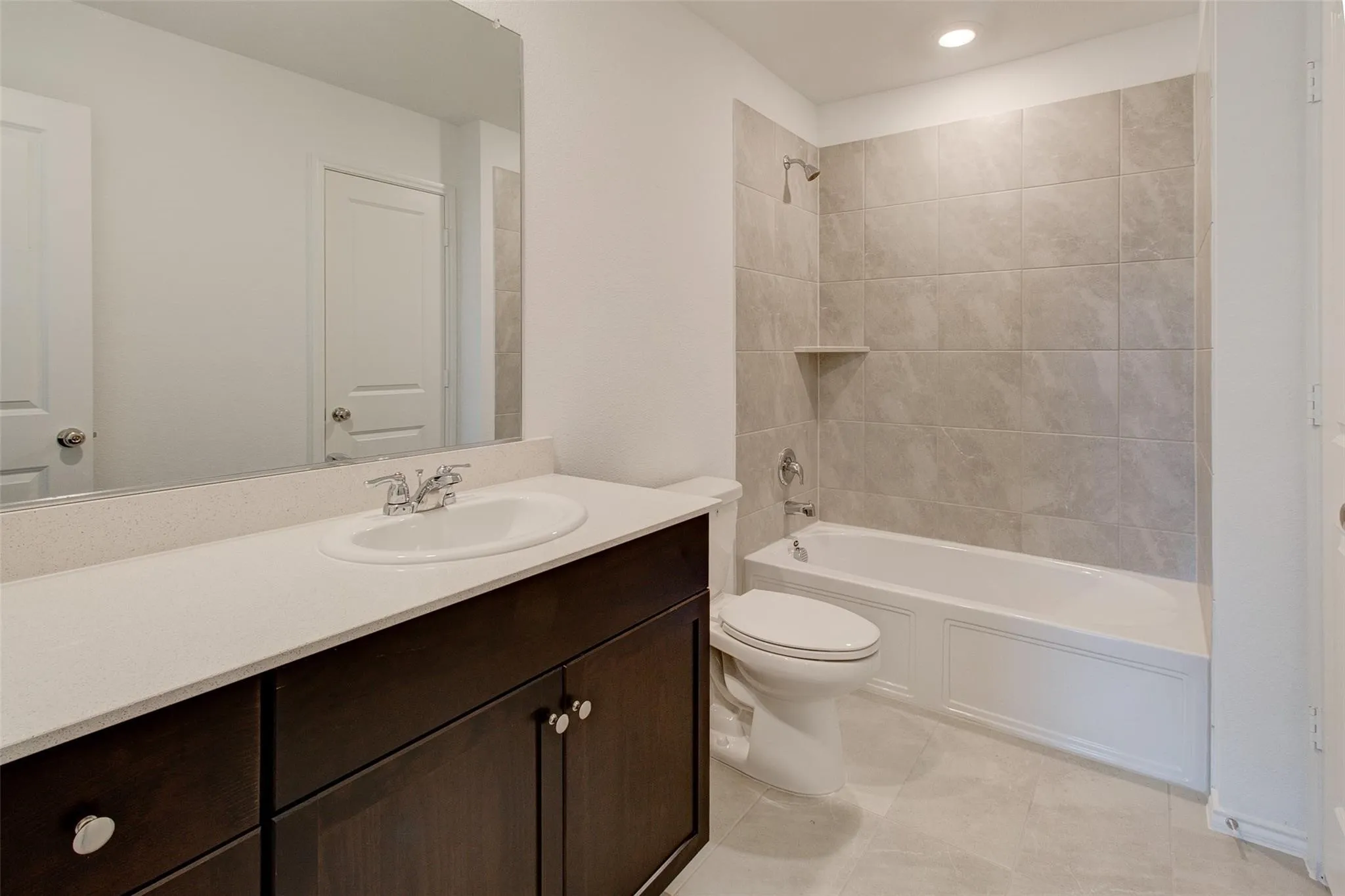 Bathroom featuring a dark wood vanity with a white countertop and undermount sink, a white tub and shower combination with light-toned tile surround, and recessed lighting