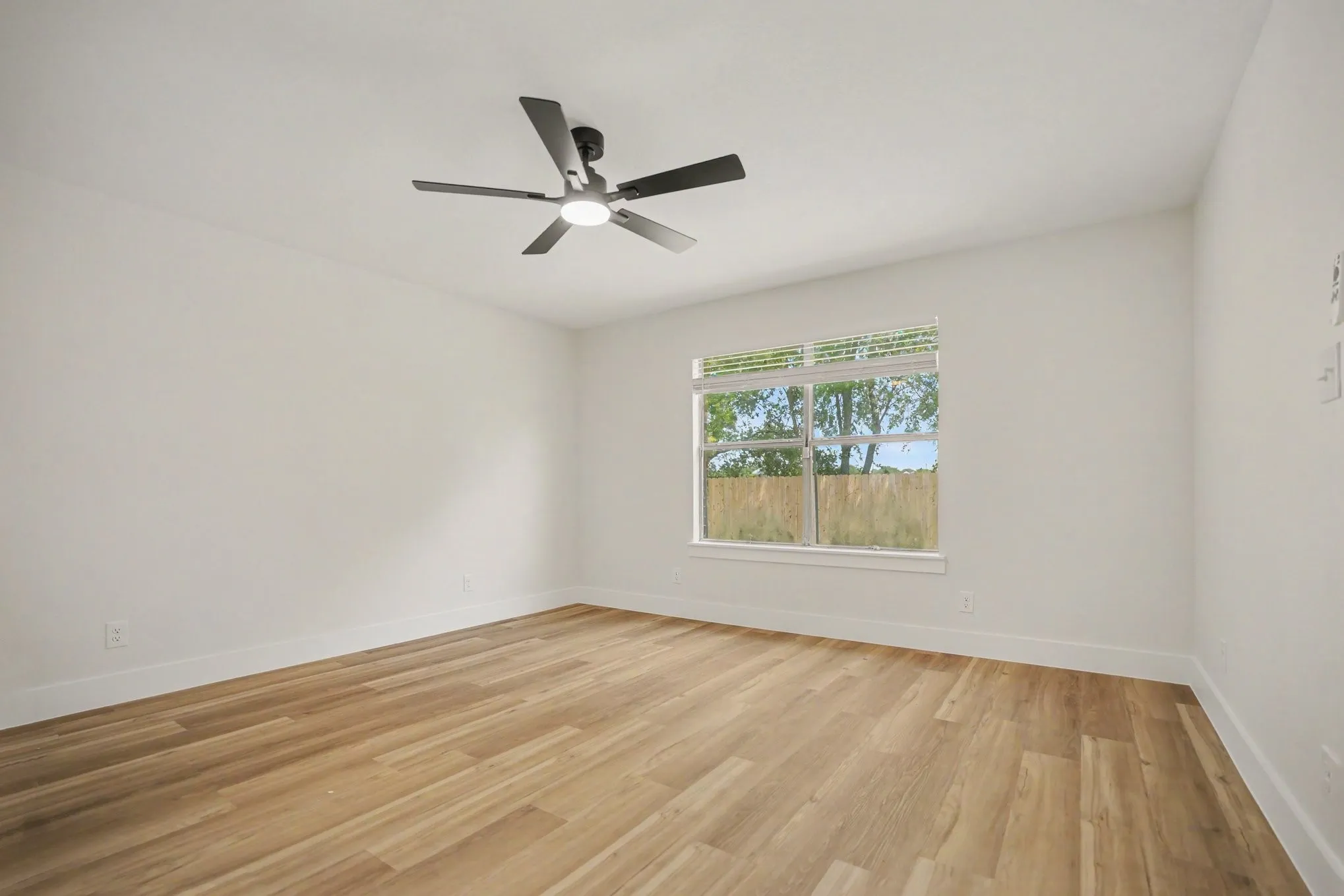 Spacious primary bedroom with wood-finish flooring, white walls, and a contemporary ceiling fan