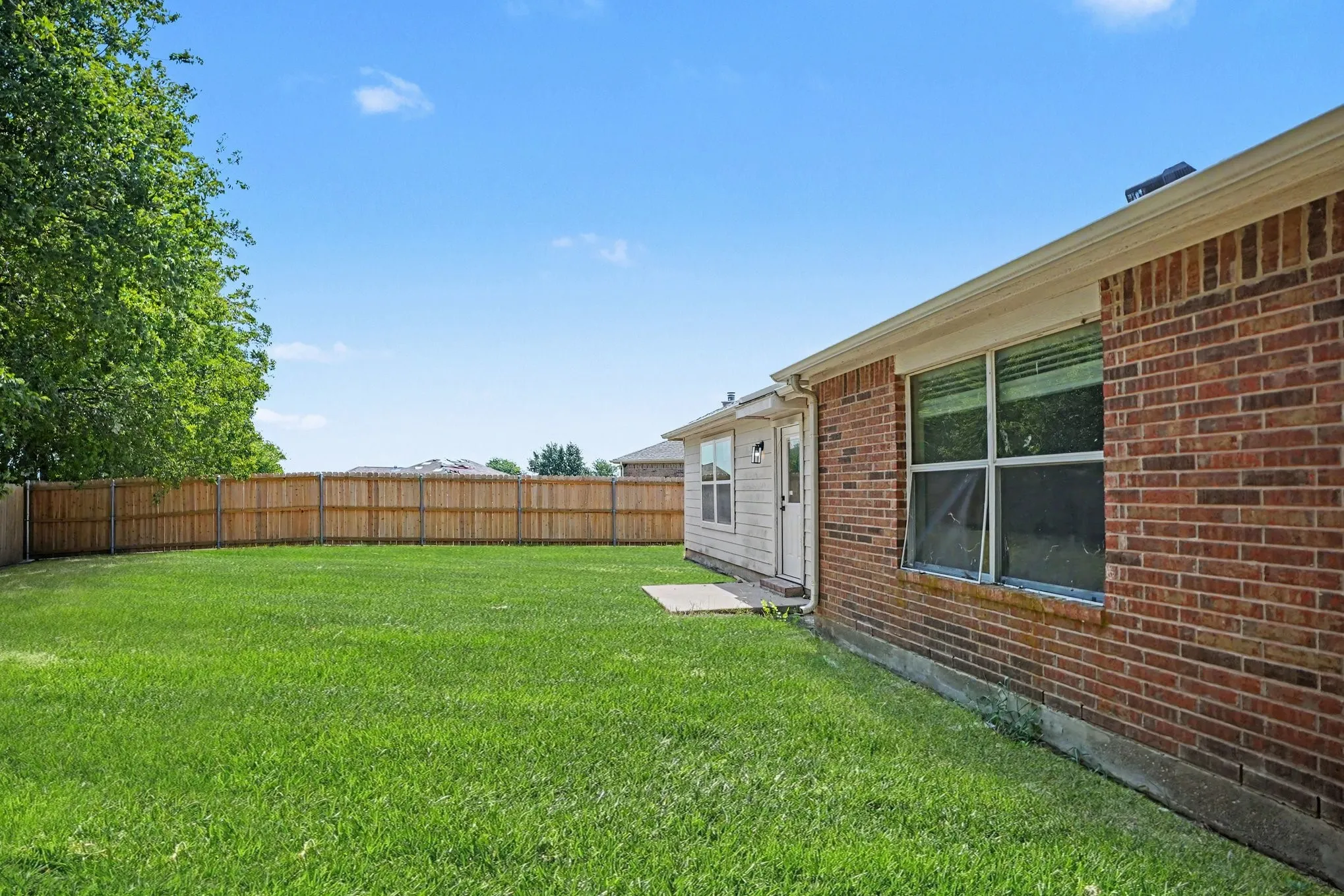 Expansive backyard featuring a manicured lawn, full privacy fence, and concrete patio