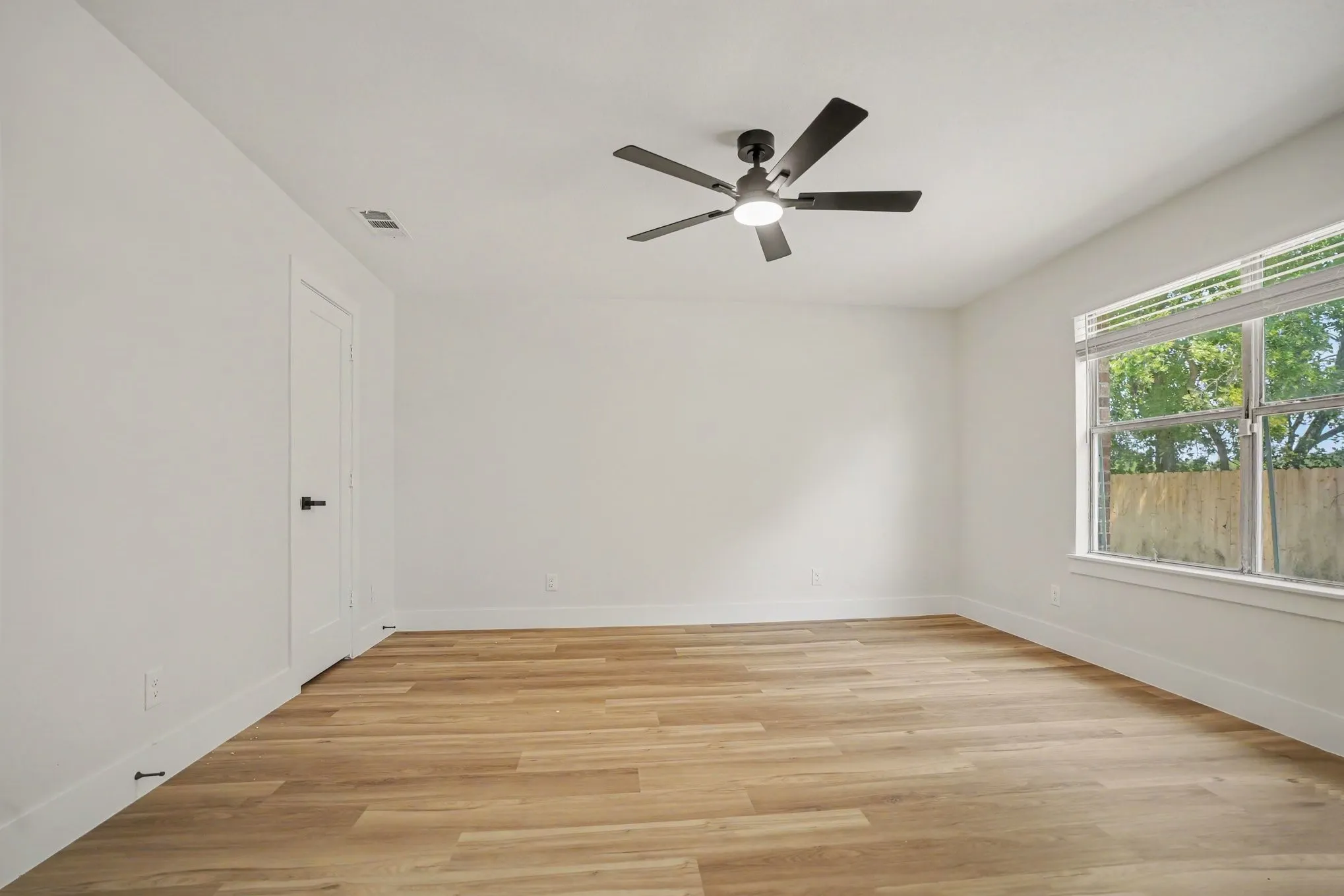 Spacious primary bedroom featuring wood-finish flooring, white walls, and a contemporary ceiling fan with integrated lighting