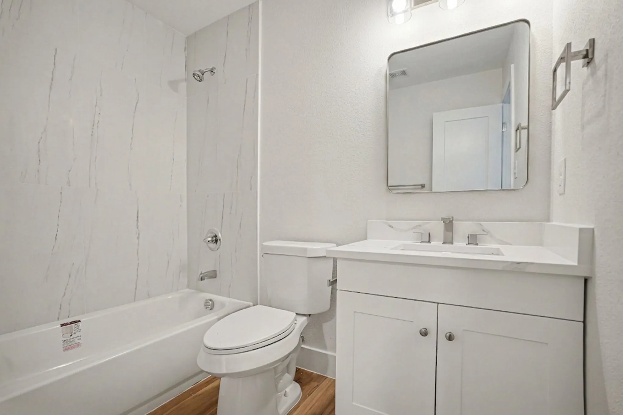 Full bathroom featuring a white bathtub with a tile surround, a toilet, and a white vanity with an integrated sink and brushed nickel faucet