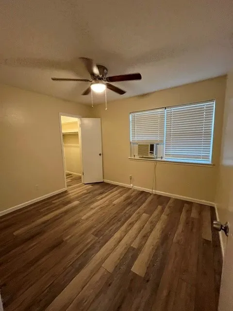 Wood-finish flooring, ceiling fan with integrated lighting, window blinds, and a window air conditioning unit