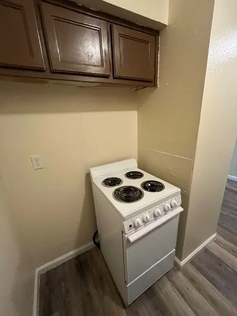 White electric range with four burners, brown overhead cabinetry, and wood-finish flooring