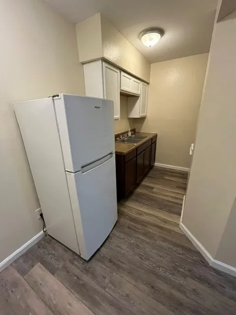 Wood-finish flooring, white upper cabinetry, brown lower cabinetry, and a neutral wall color
