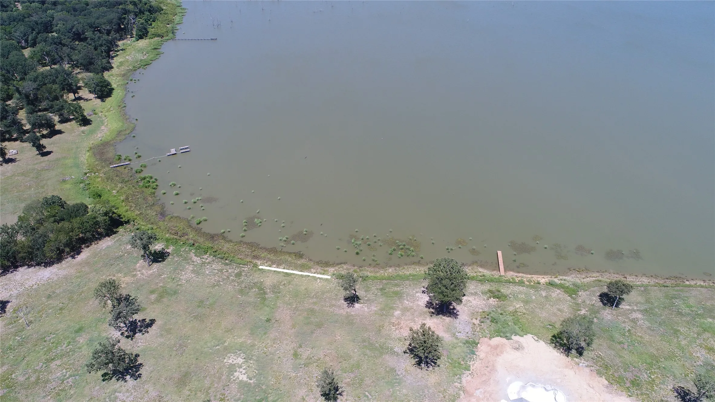 Expansive waterfront property featuring direct access to a large body of water, a natural shoreline, mature trees, and a developed land area with a small dock structure
