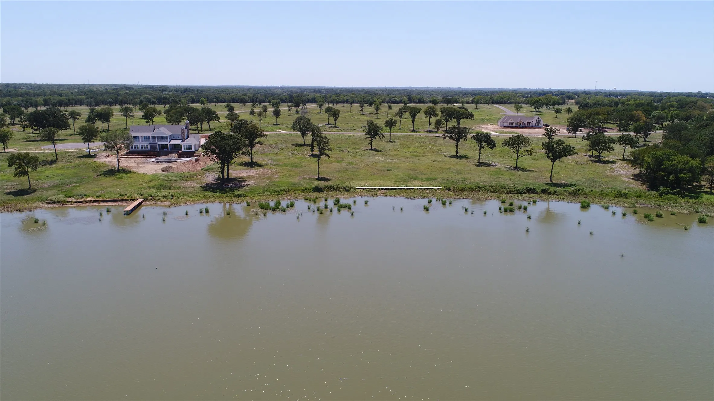 Waterfront property featuring a newly constructed residence, a private dock, and a landscape with mature trees